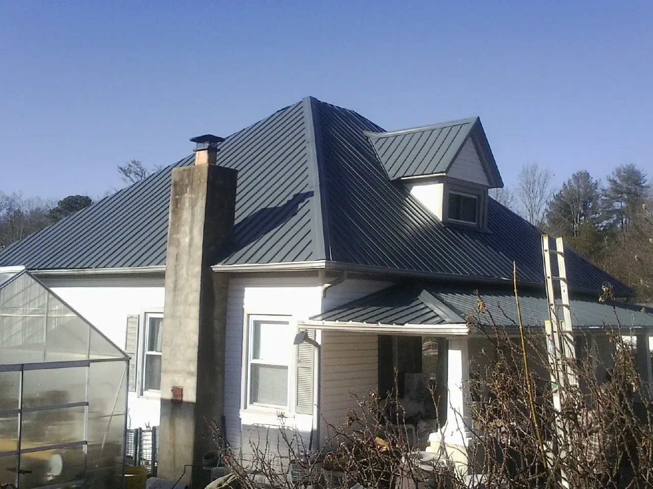 Dark blue standing seam metal roof on a white farmhouse with dormer — Slate & Tile Roof Repair by Roofing Brothers in Darden