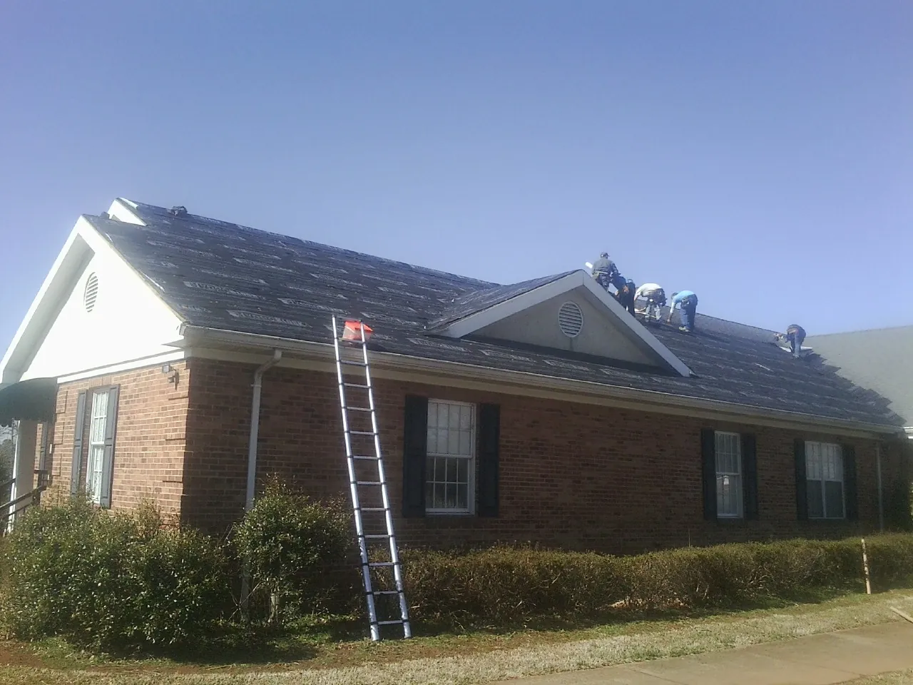 Crew tearing shingles off a brick ranch roof with a ladder set — Emergency Roof Repair work by our crew in Darden