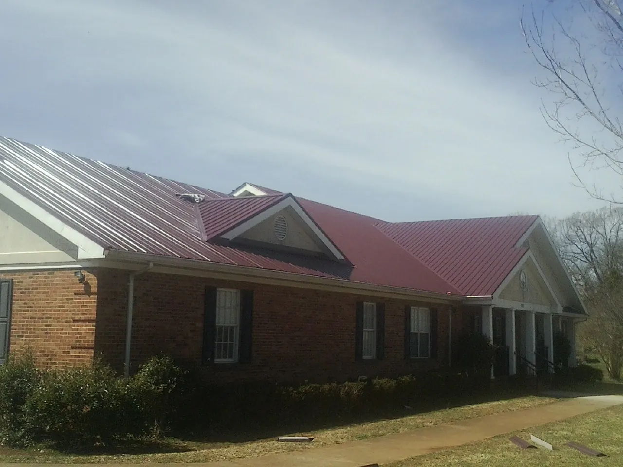 Red metal roof with gabled entries on a long brick building, from a Hail Damage Roof Repair job in Darden