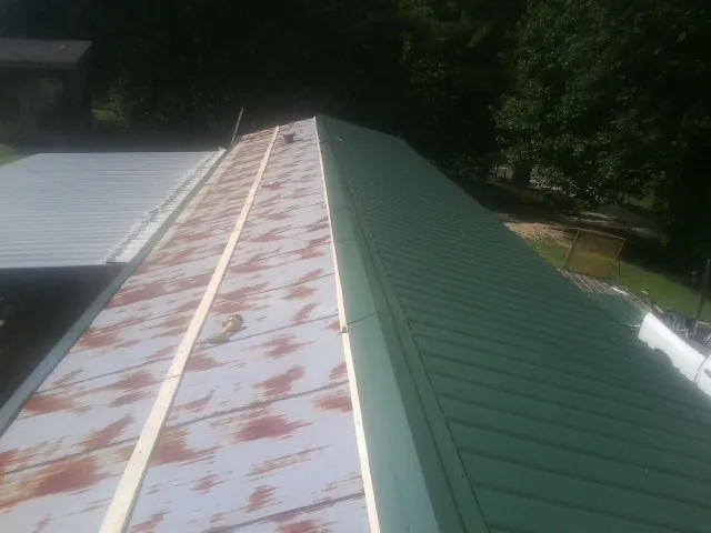 Old rusted panels beside newly installed green metal roofing — Wind Damage Roof Repair by Roofing Brothers in Darden