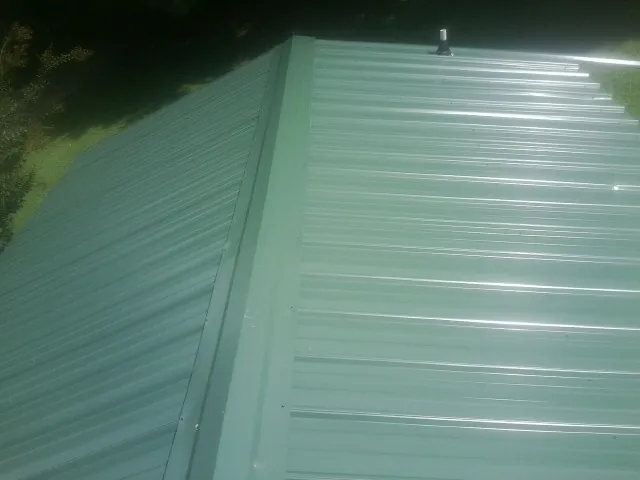 New green metal panels meeting at the ridge of a roof — Flat Roof Repair work by our crew in Darden
