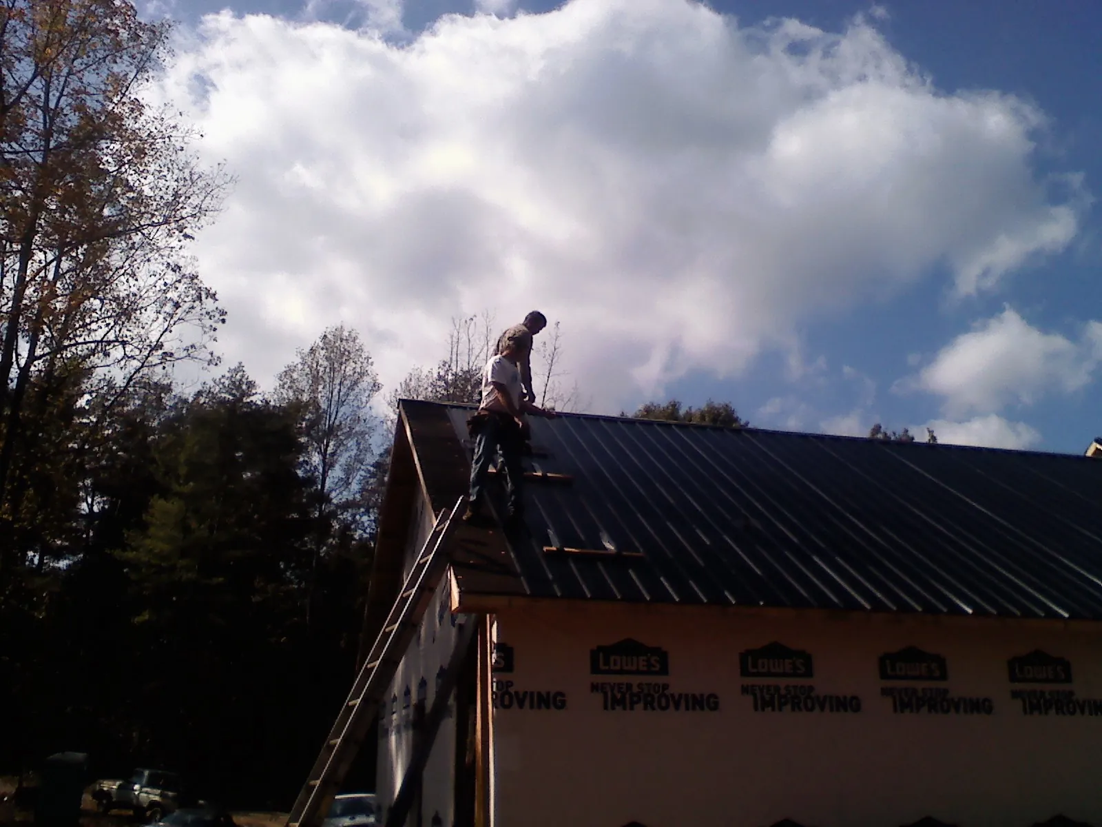 Roofer fastening dark metal panels high against a cloudy sky, from a Roof Inspection job in Darden