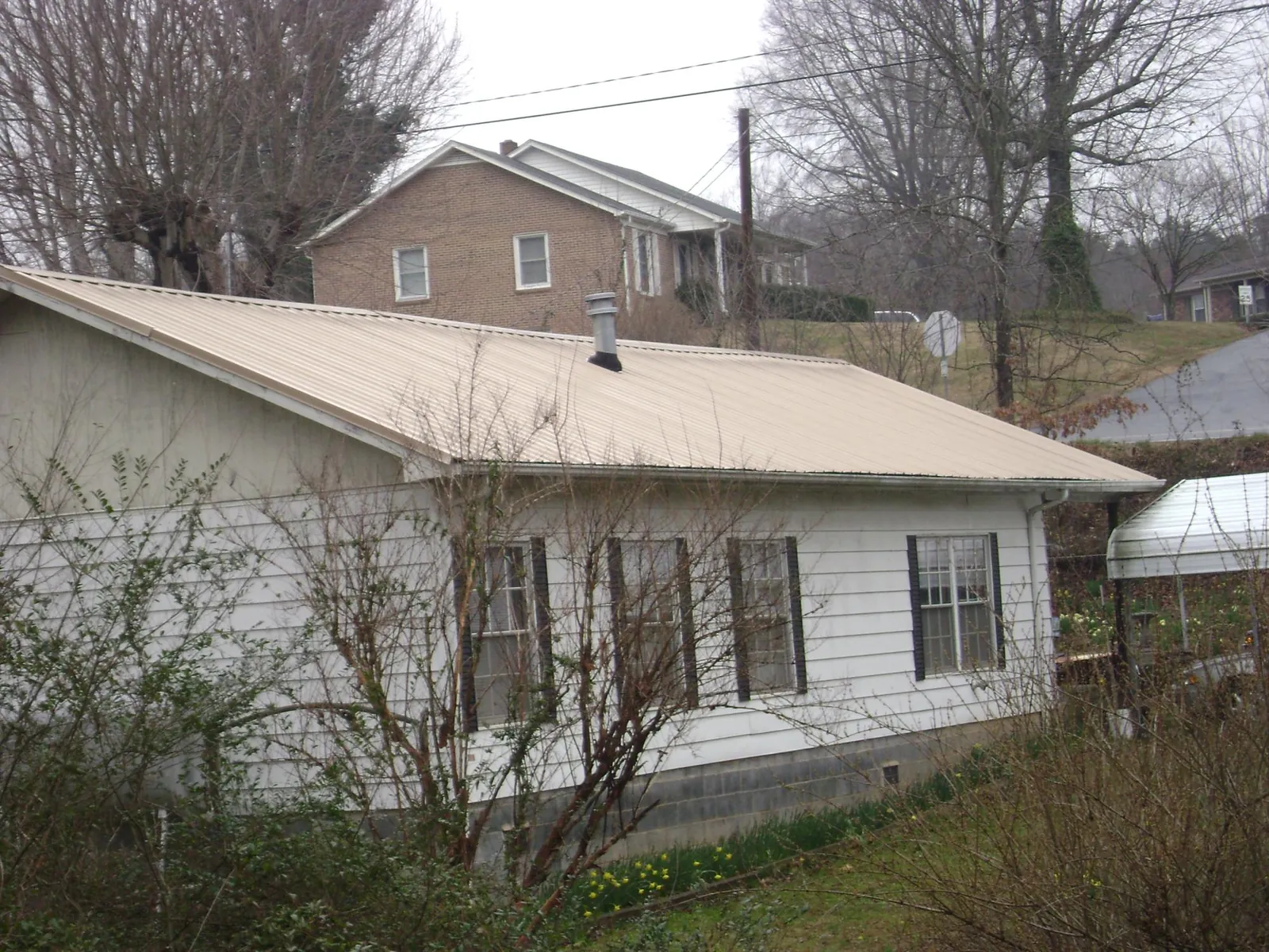 Tan metal roof on a white sided house set into a hillside — Commercial Roofing by Roofing Brothers in Darden