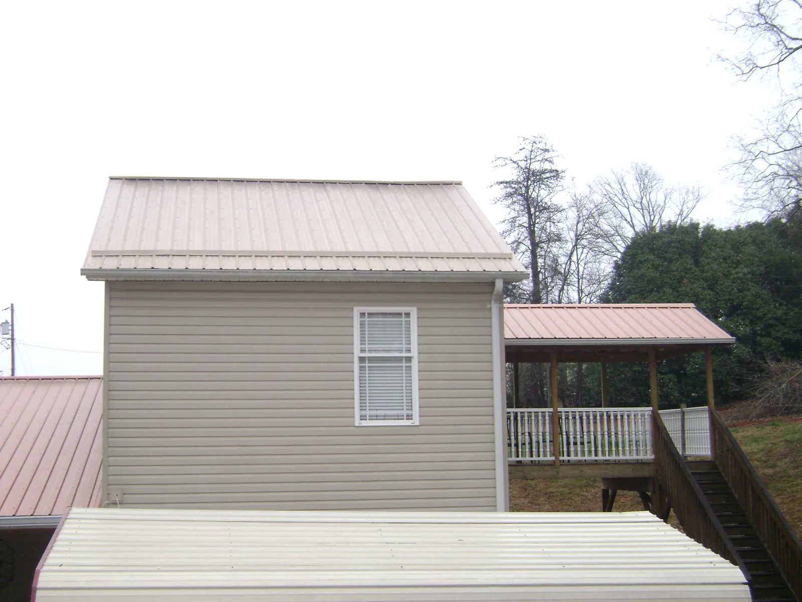 Tan metal roofs on a two story addition and attached porch, from a Roof Replacement job in Darden